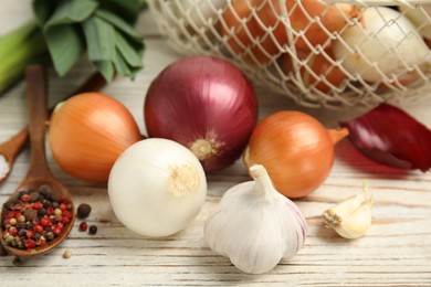 Fresh onion bulbs, leek, garlic and peppers mix on white wooden table, closeup