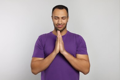Photo of African American man with clasped hands praying to God on light grey background
