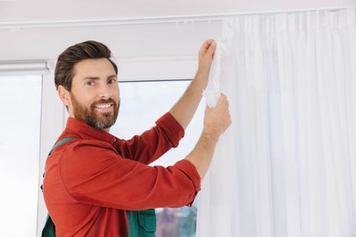 Photo of Worker in uniform hanging window curtain indoors