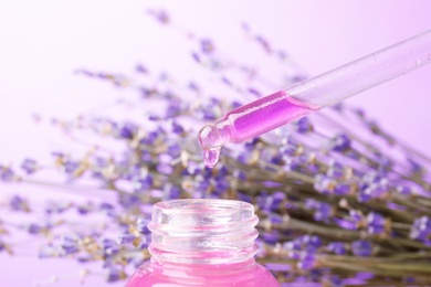 Photo of Dripping natural lavender oil into bottle against blurred background, closeup