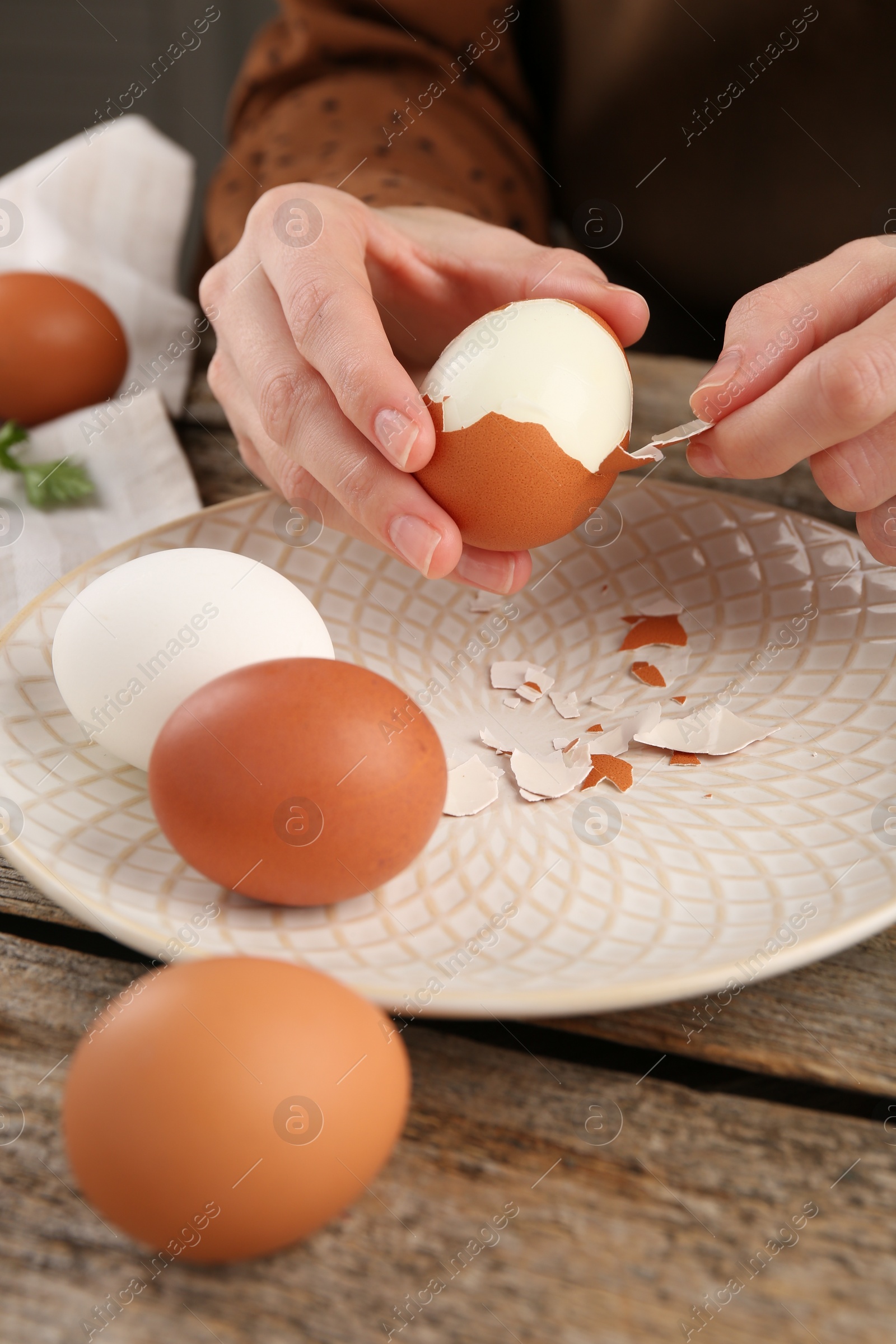 Photo of Woman peeling boiled egg at wooden table, closeup