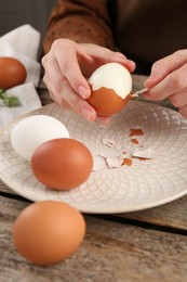 Woman peeling boiled egg at wooden table, closeup
