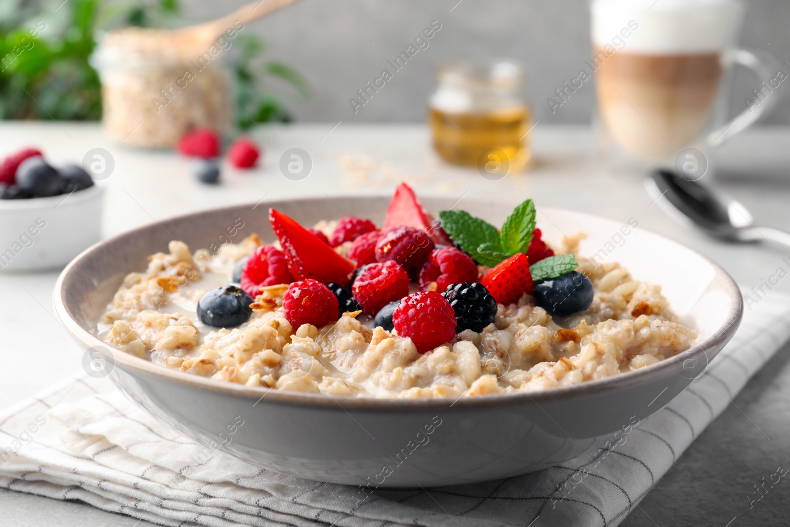 Photo of Bowl of oatmeal porridge served with berries on light grey table, closeup