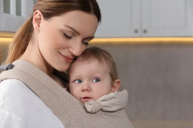 Photo of Mother holding her child in sling (baby carrier) at home, space for text