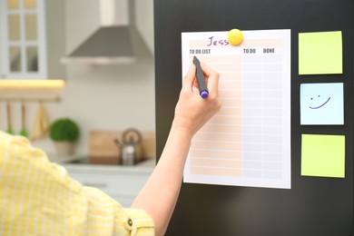 Photo of Woman writing to do list on refrigerator door in kitchen, closeup