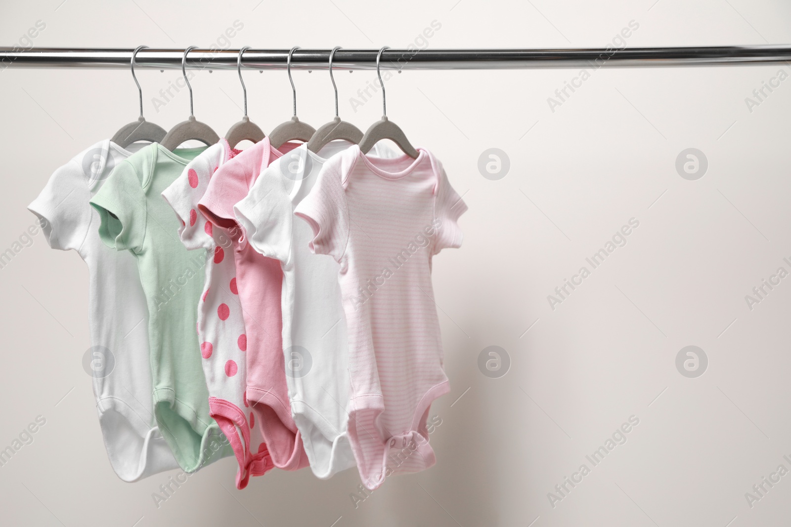 Photo of Baby bodysuits hanging on rack near white wall. Space for text