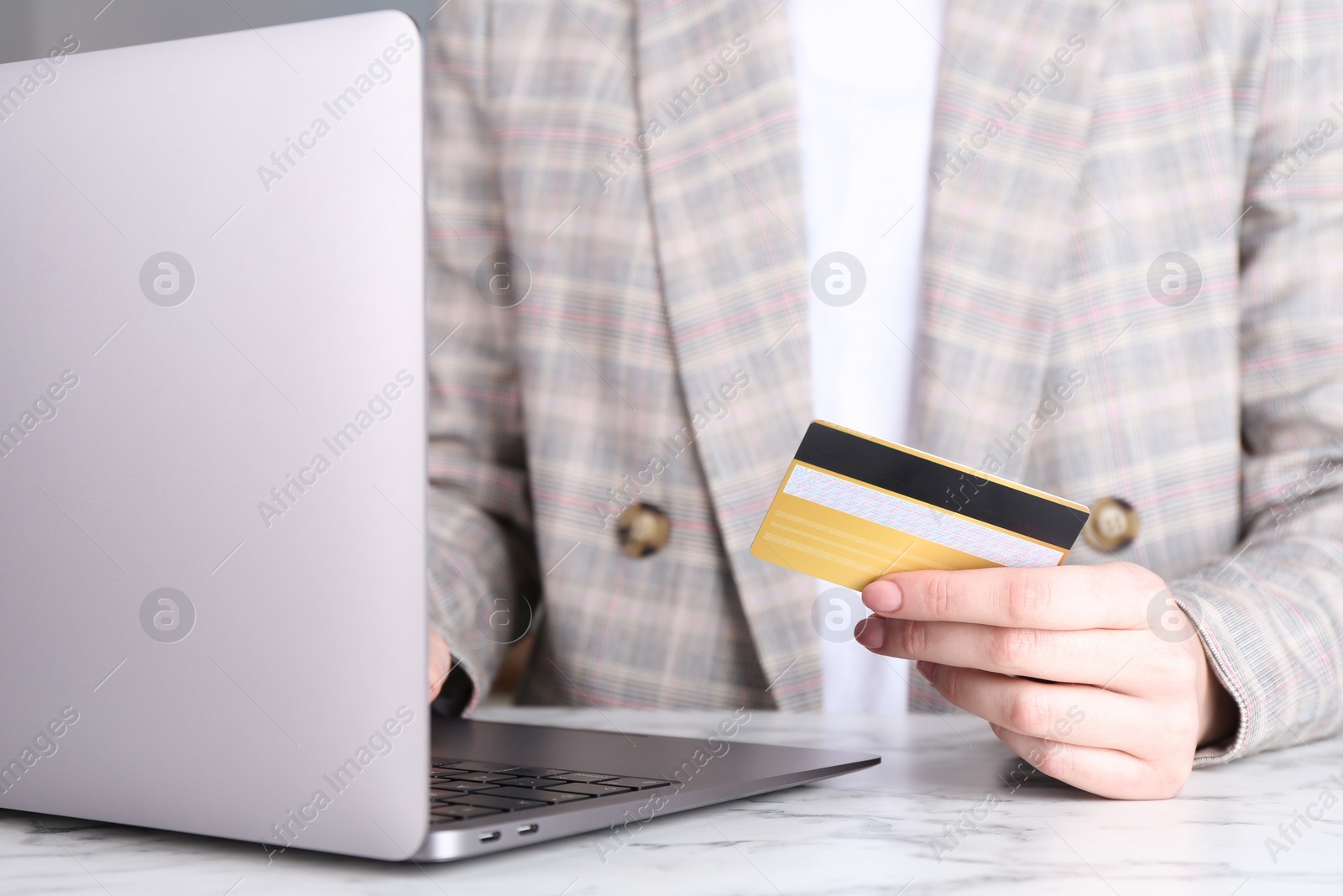 Photo of Online payment. Woman with laptop and credit card at white marble table, closeup