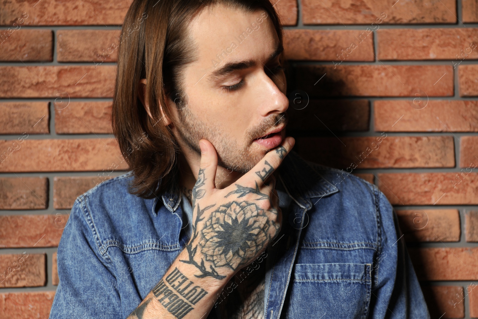 Photo of Young man with tattoos on hand near brick wall