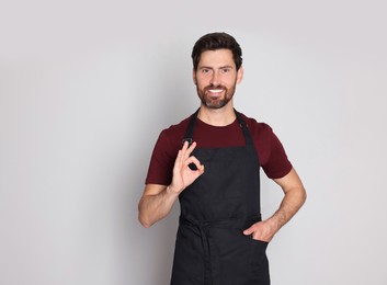 Photo of Professional hairdresser wearing apron showing ok gesture on light grey background, space for text
