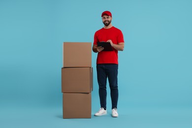 Happy courier with clipboard and stack of parcels on light blue background