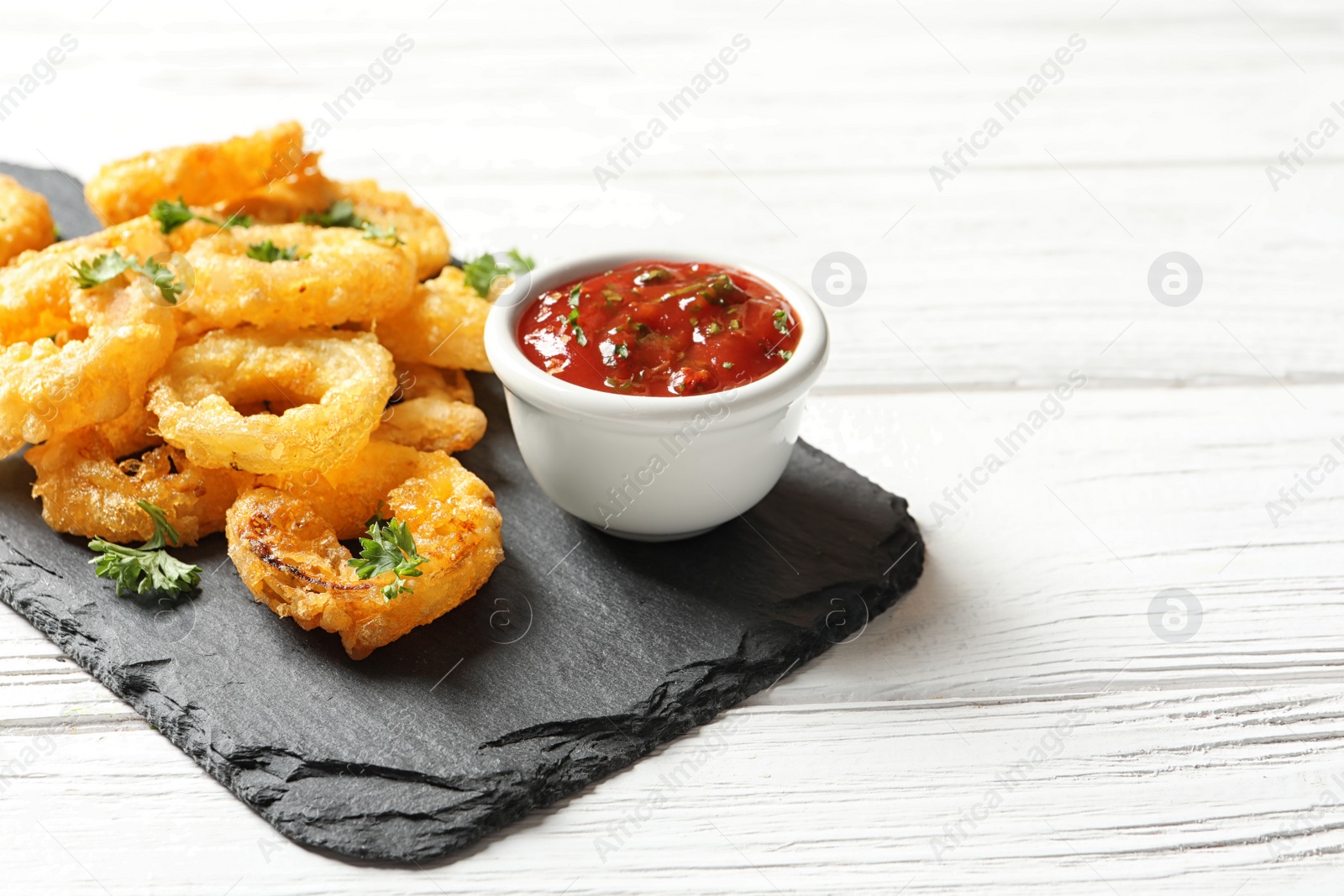Photo of Homemade crunchy fried onion rings with tomato sauce on wooden table. Space for text