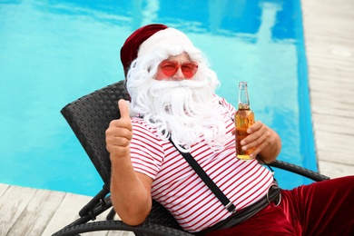 Photo of Authentic Santa Claus with bottle of beer near pool at resort