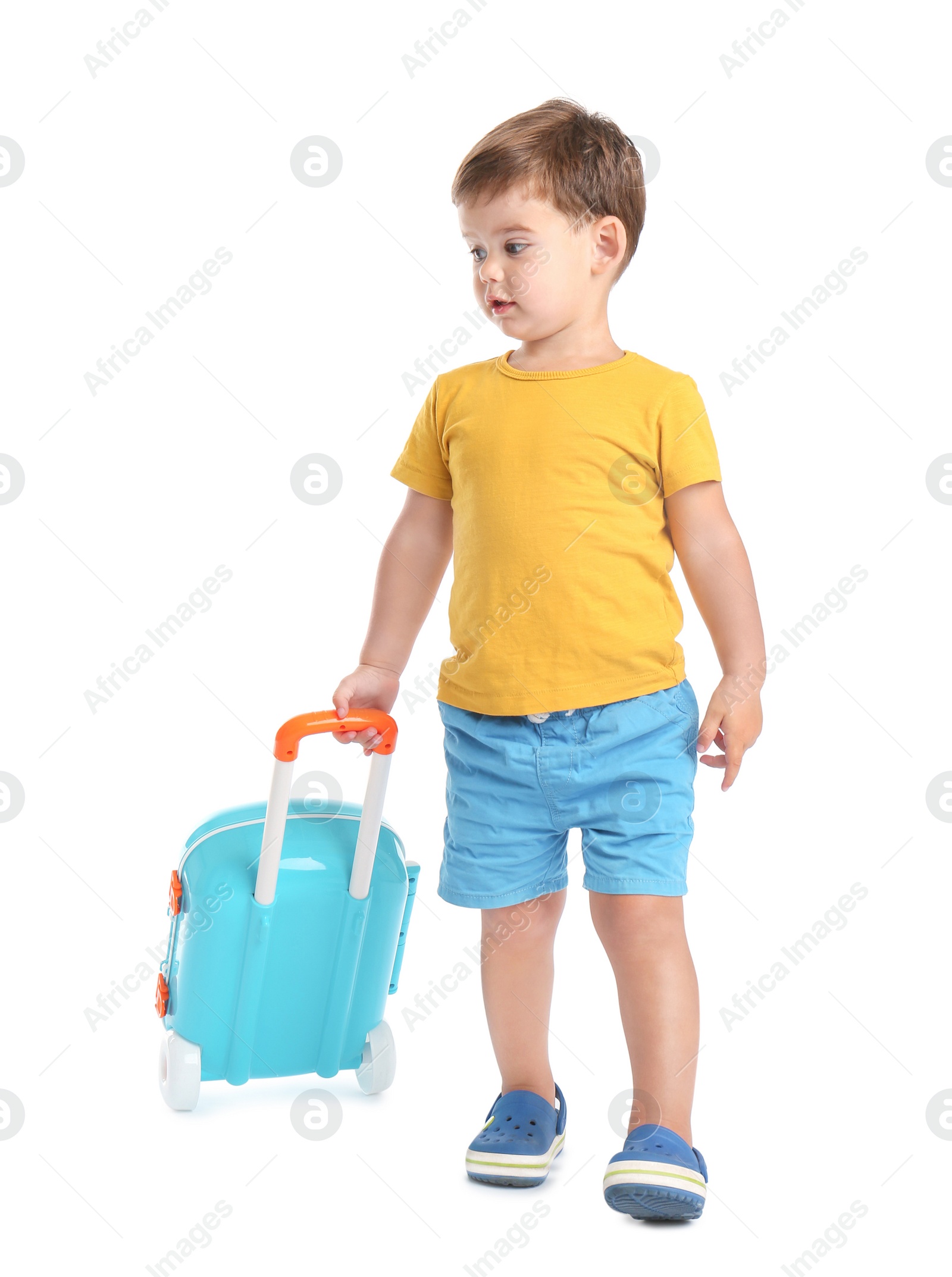 Photo of Cute little boy walking with blue suitcase on white background