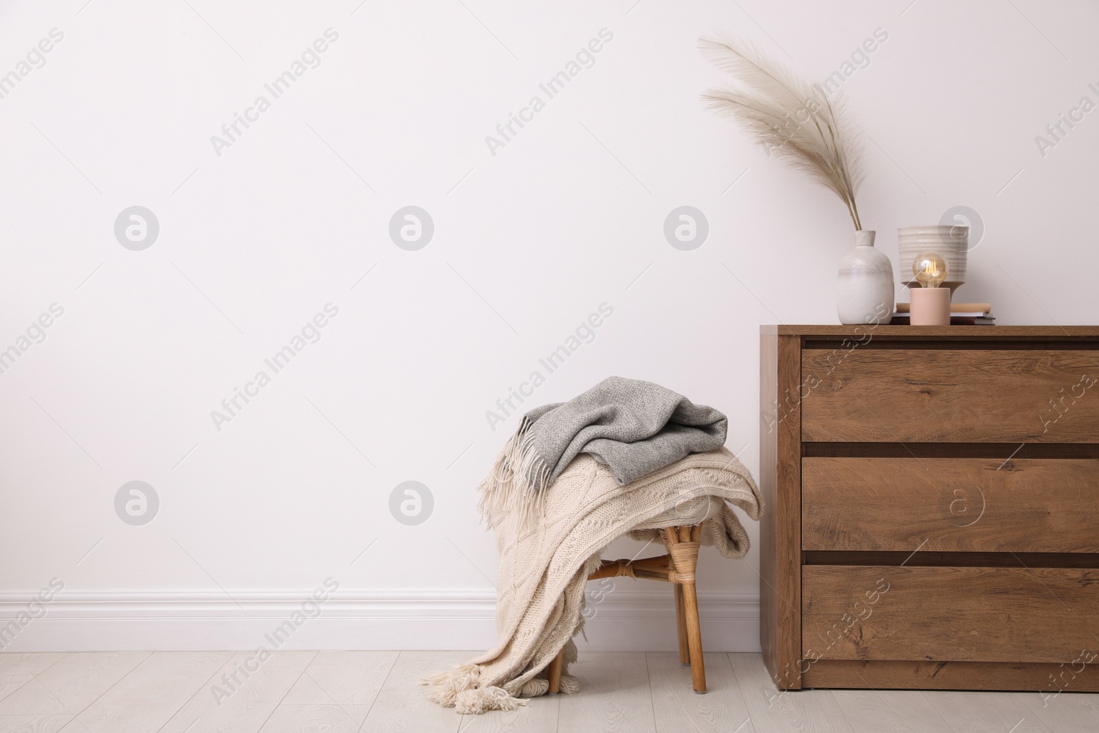 Photo of Modern chest of drawers and stool near white wall in room. Space for text