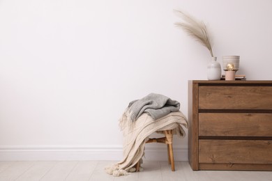 Photo of Modern chest of drawers and stool near white wall in room. Space for text
