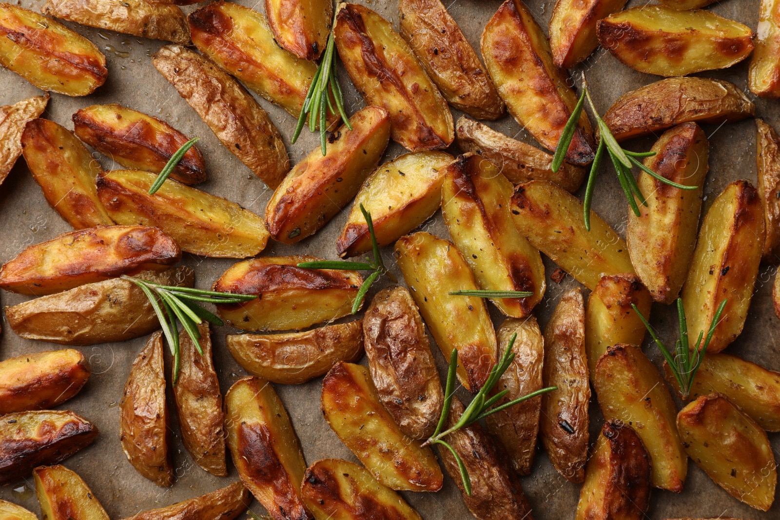 Photo of Tasty baked potato and aromatic rosemary on parchment paper, flat lay