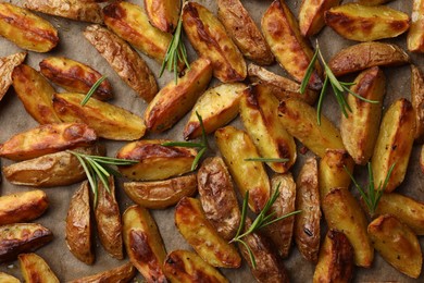 Tasty baked potato and aromatic rosemary on parchment paper, flat lay