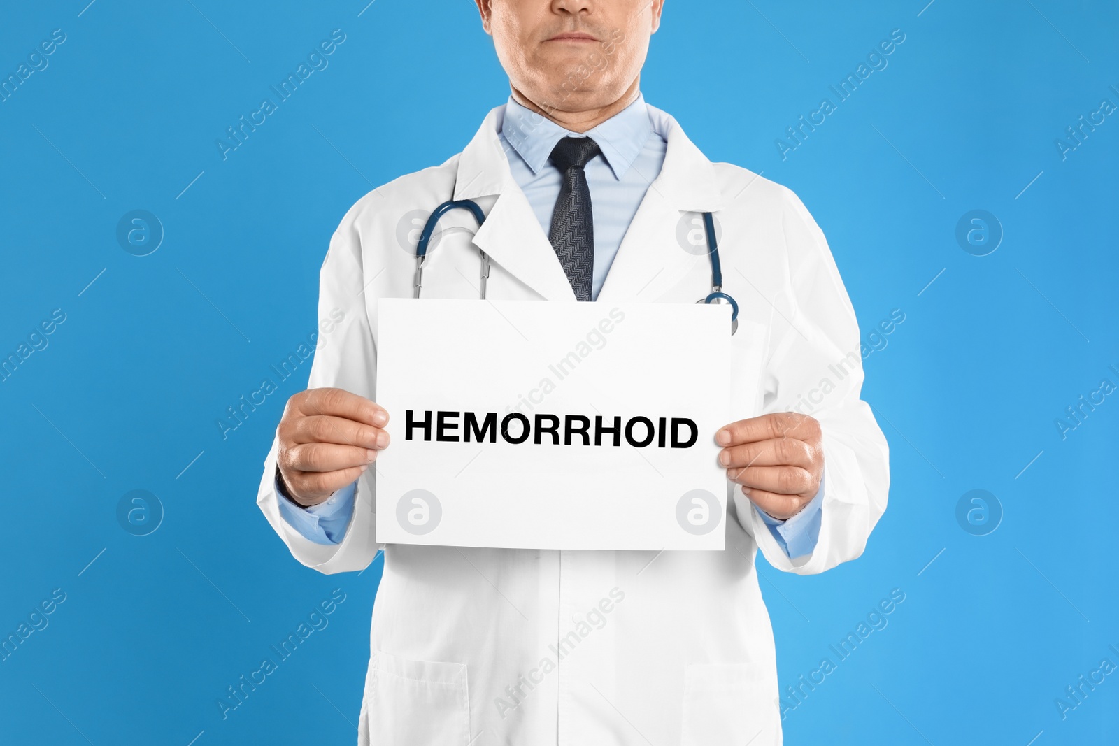 Photo of Doctor holding sign with word HEMORRHOID on blue background, closeup