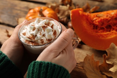 Photo of Woman holding tasty pumpkin latte at wooden table, closeup