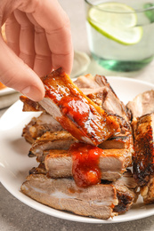 Woman with grilled ribs at light grey table, closeup