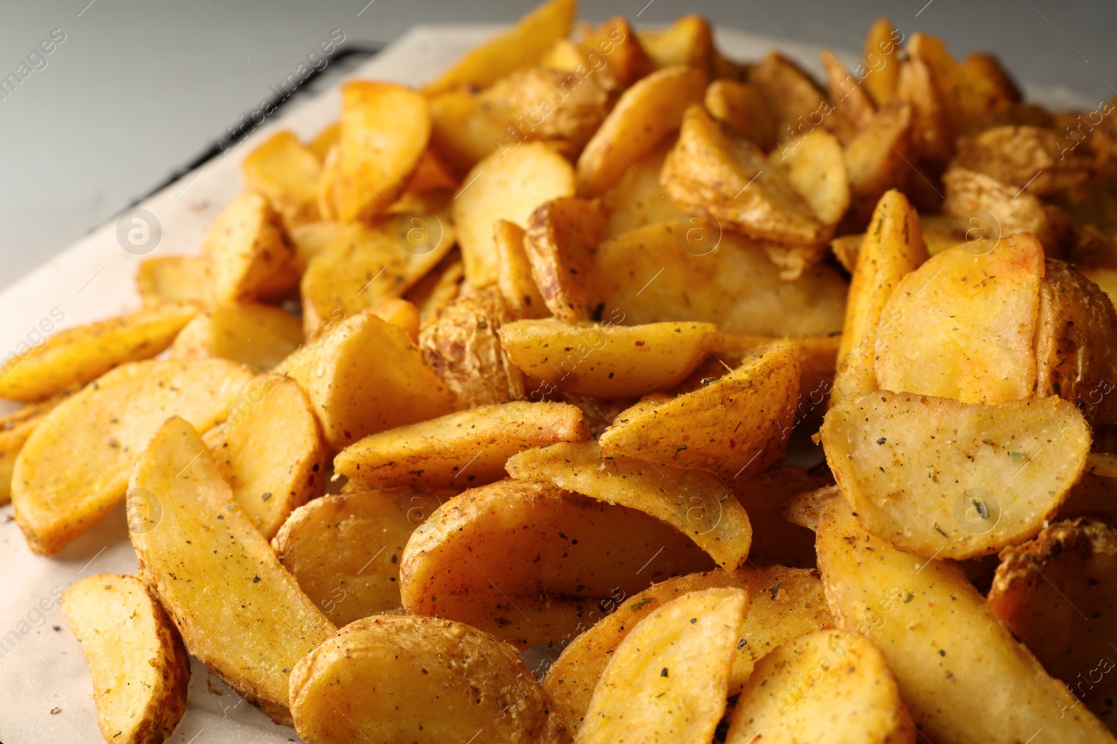 Photo of Delicious oven baked potatoes on parchment, closeup