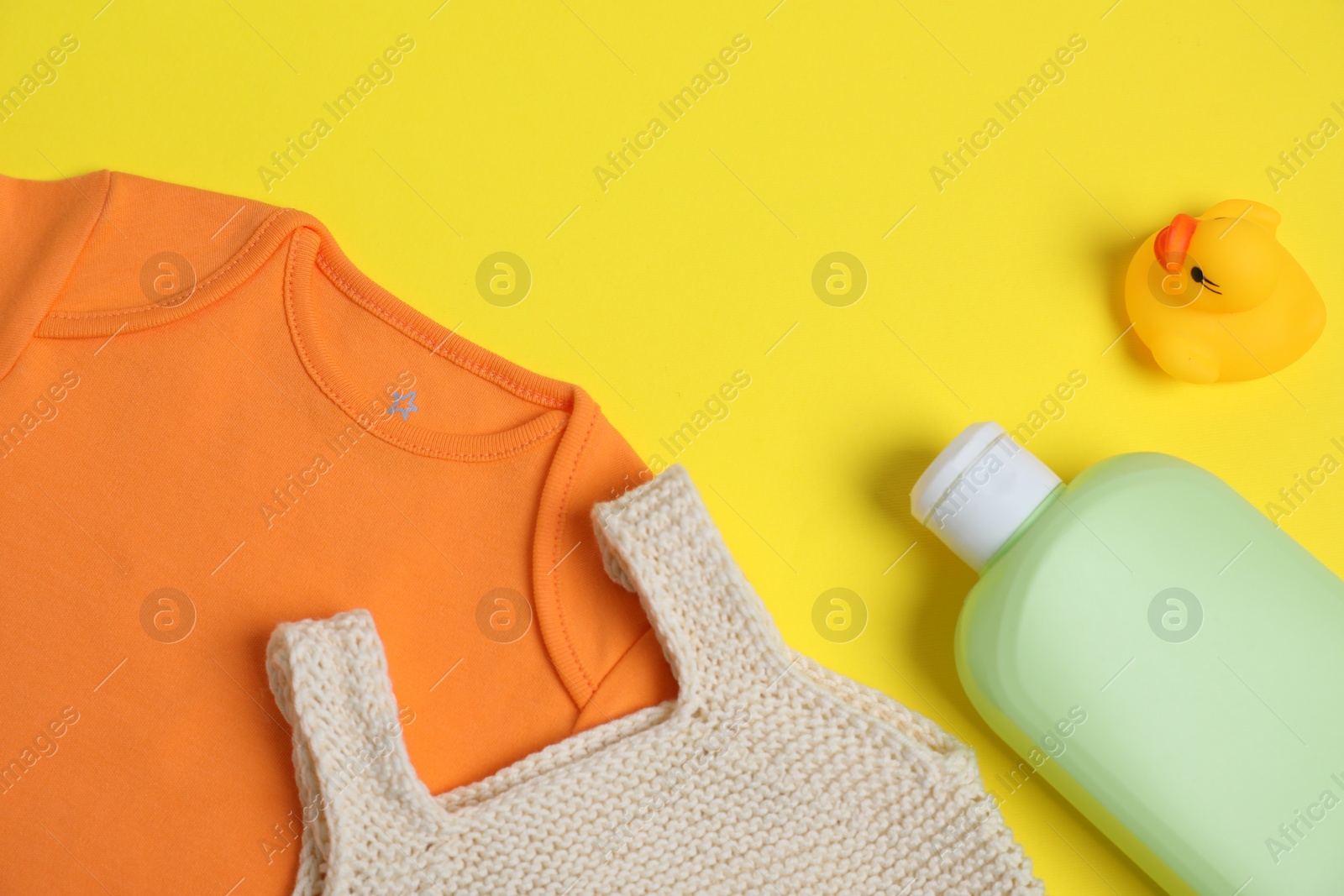 Photo of Bottles of laundry detergents, baby clothes and rubber duck on yellow background, flat lay. Space for text