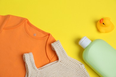 Photo of Bottles of laundry detergents, baby clothes and rubber duck on yellow background, flat lay. Space for text