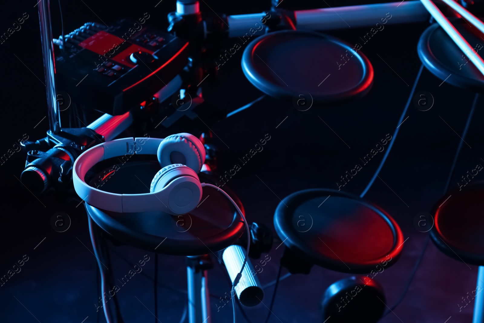 Photo of Modern electronic drum kit with headphones on dark background, color toned. Musical instrument