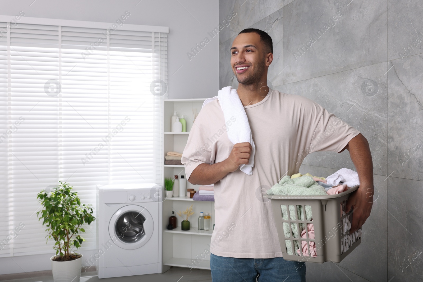 Photo of Happy man with basket full of laundry in bathroom. Space for text