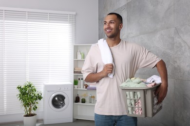 Photo of Happy man with basket full of laundry in bathroom. Space for text