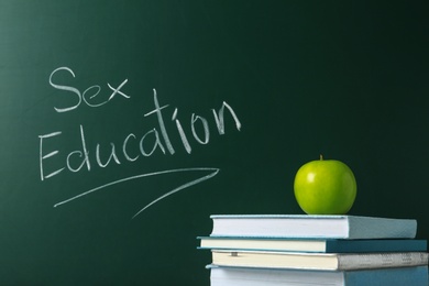 Photo of Books and apple near chalkboard with phrase "Sex education"