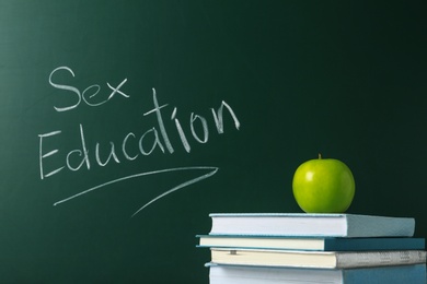 Books and apple near chalkboard with phrase "Sex education"