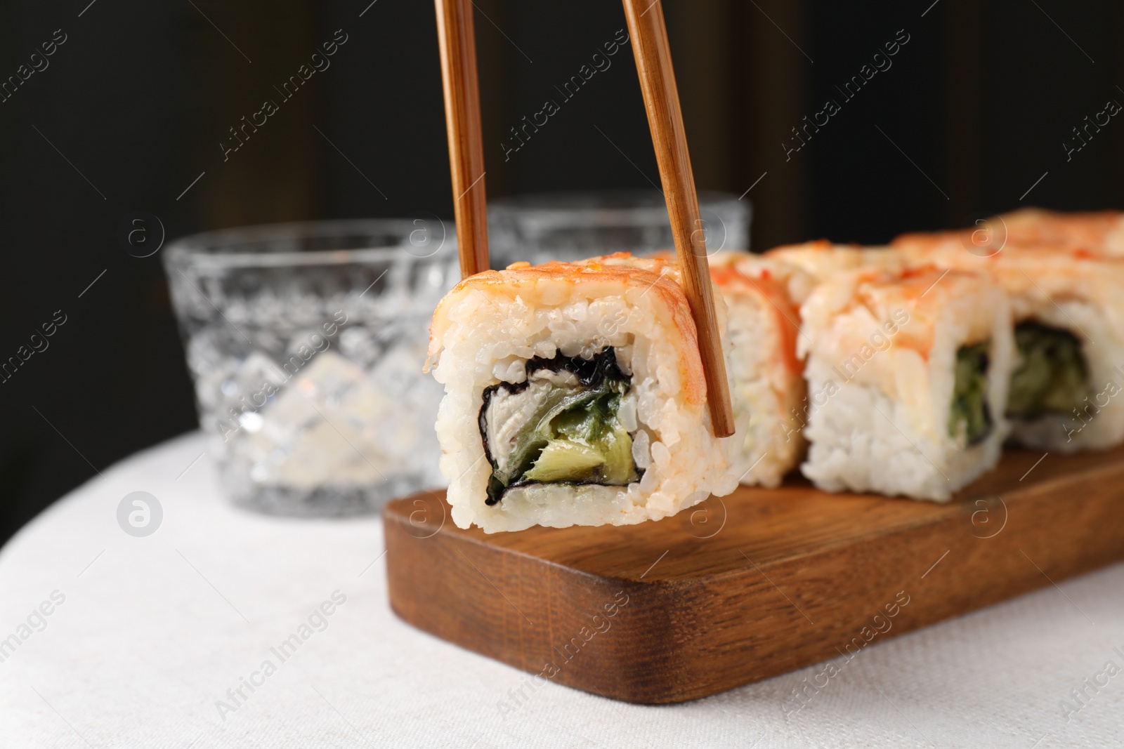 Photo of Holding delicious sushi roll with chopsticks, closeup