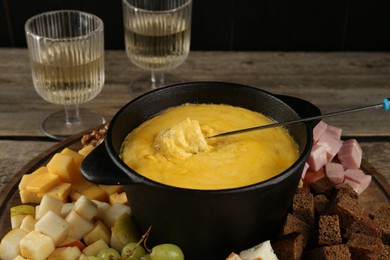 Photo of Fondue pot with melted cheese, glasses of wine and different products on wooden table, closeup