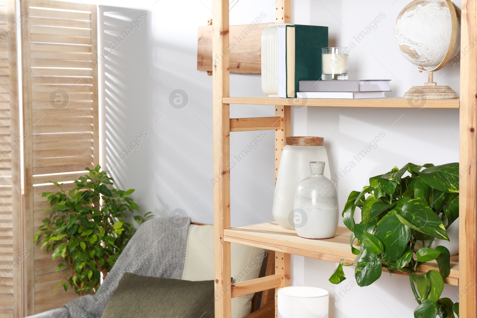 Photo of Wooden shelving unit with home decor, folding screen and armchair near light wall in room. Interior design