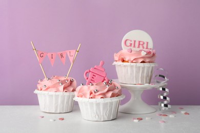 Photo of Baby shower cupcakes with pink cream and toppers on white table against violet background