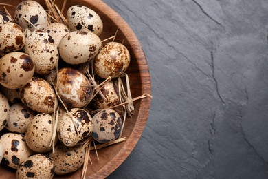 Photo of Bowl with quail eggs and straw on black table, top view. Space for text