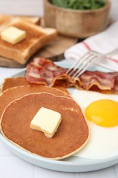 Tasty pancakes served with fried egg and bacon on white tiled table, closeup