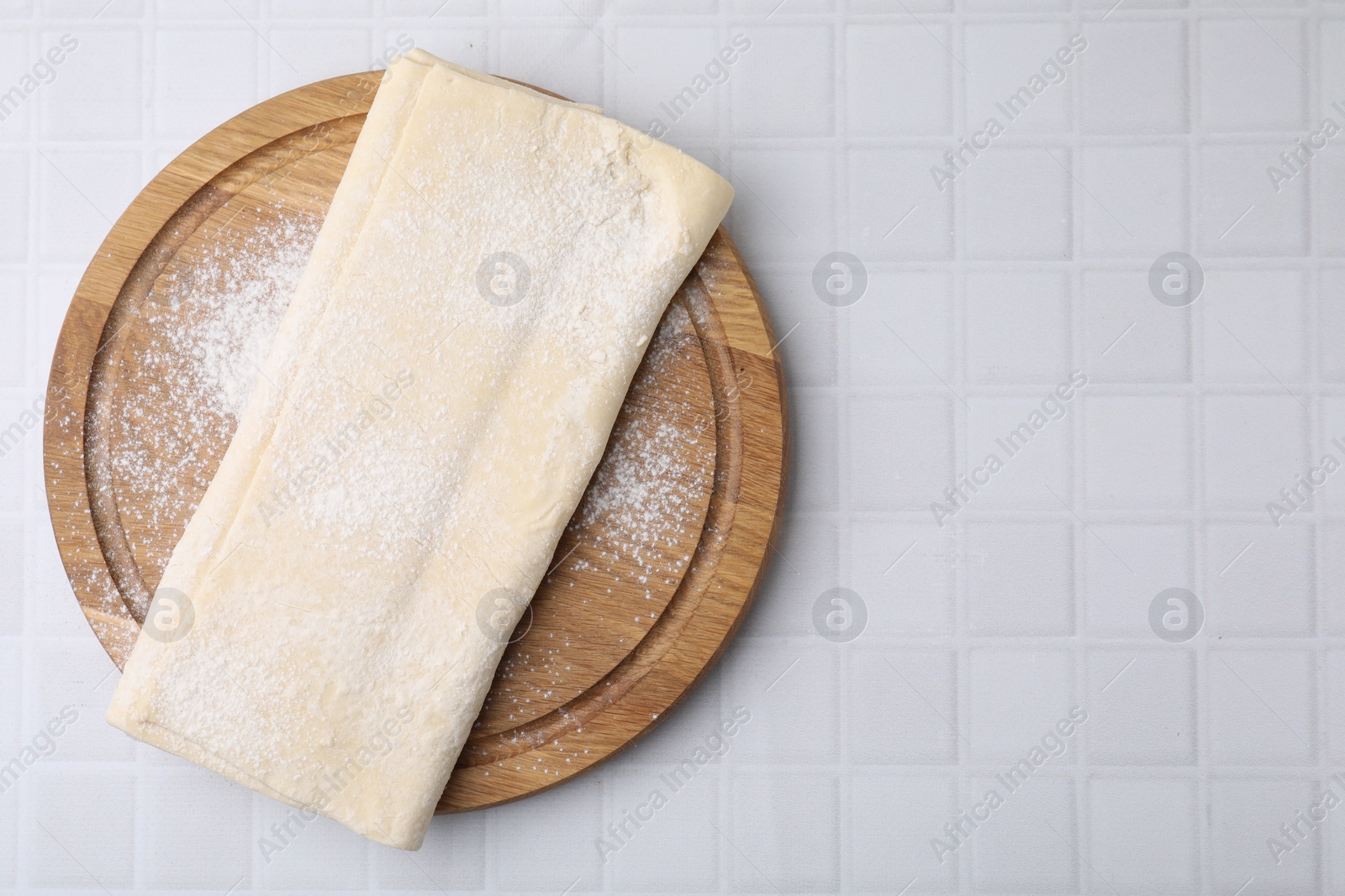 Photo of Raw puff pastry dough on white tiled table, top view. Space for text