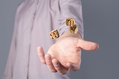 Image of Man throwing golden dice on grey background, closeup