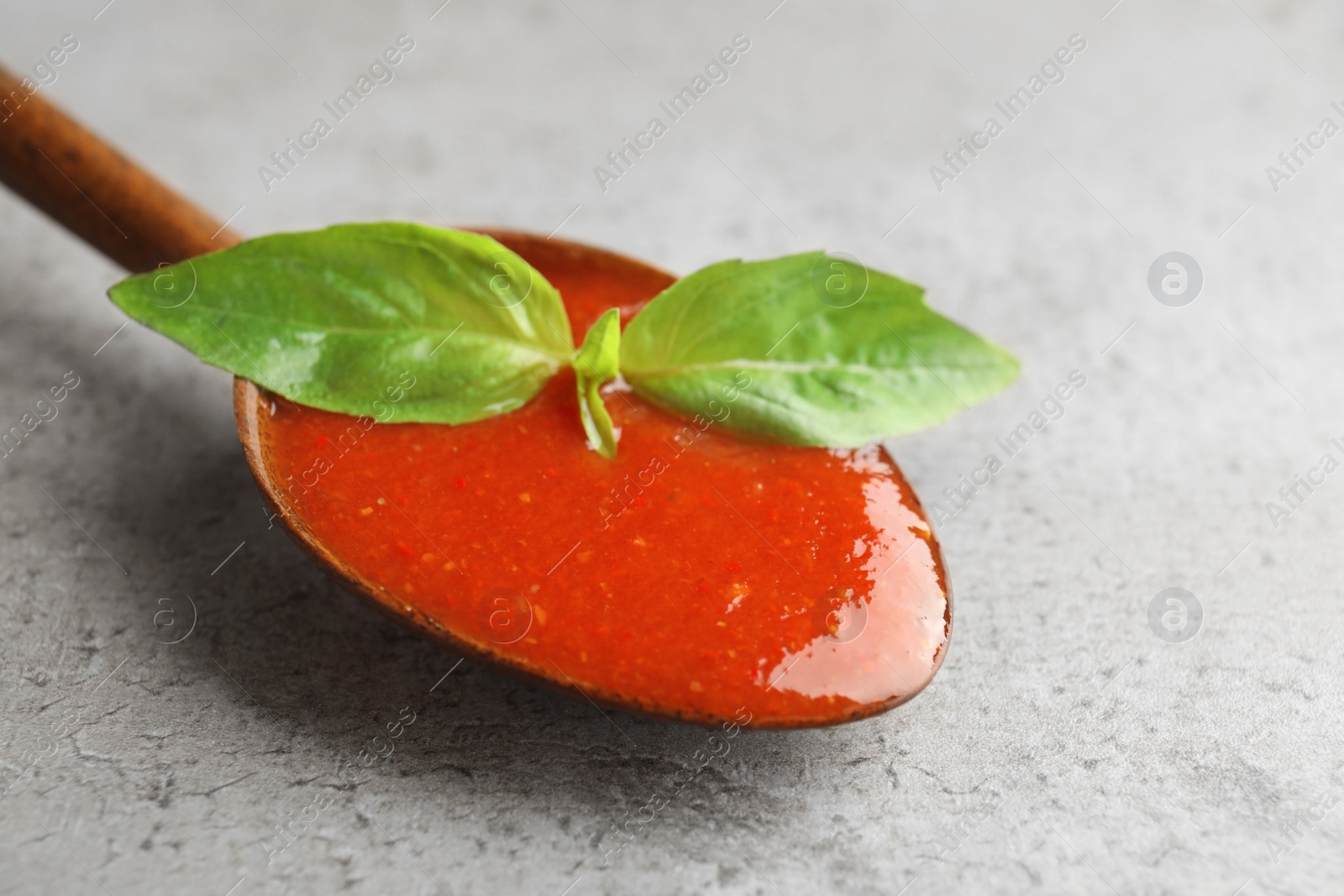 Photo of Spoon of tomato sauce on grey table, closeup. Space for text