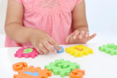 Photo of Little girl playing with colorful puzzles at white table, closeup. Educational toy