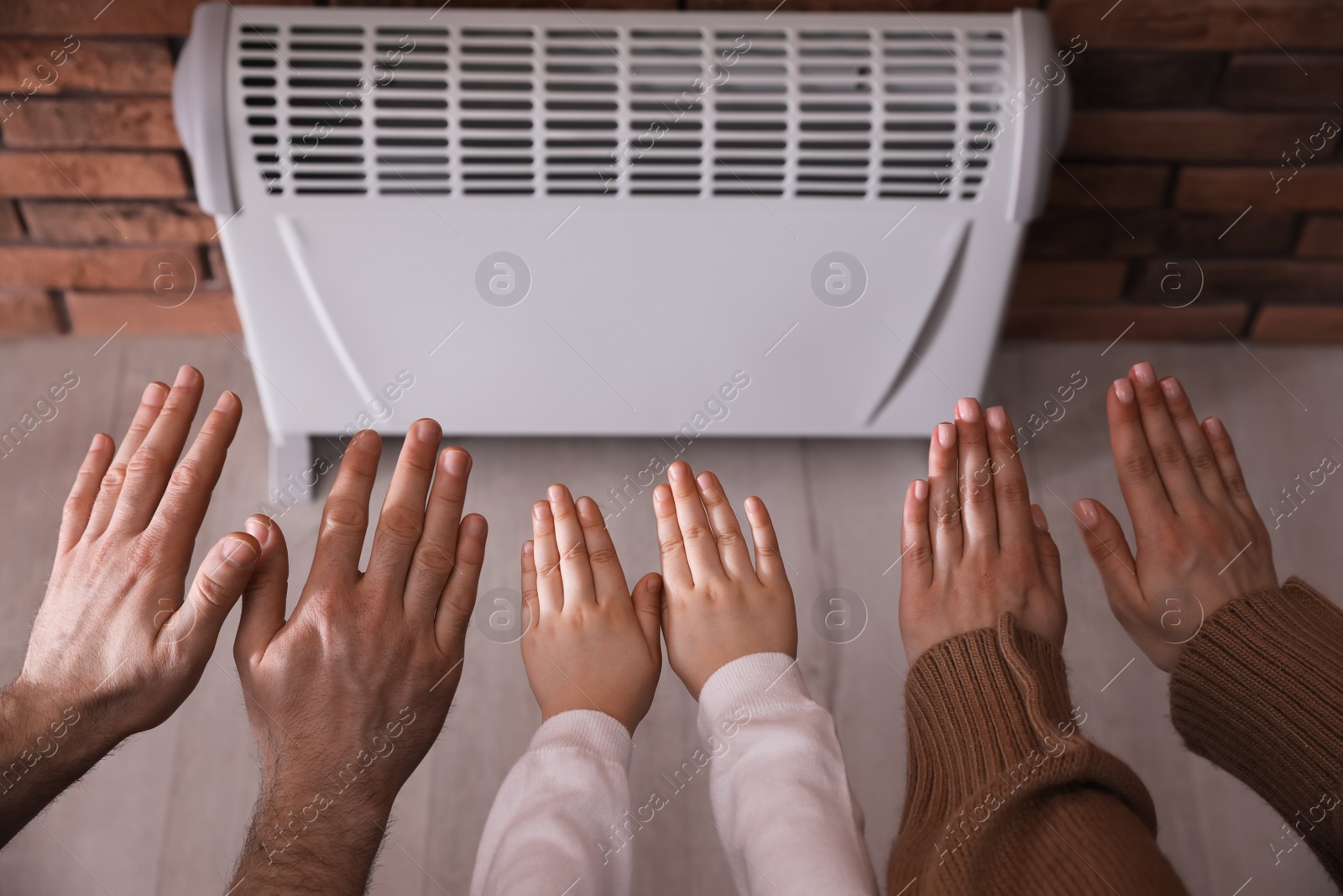 Photo of Family warming hands near electric heater at home, closeup