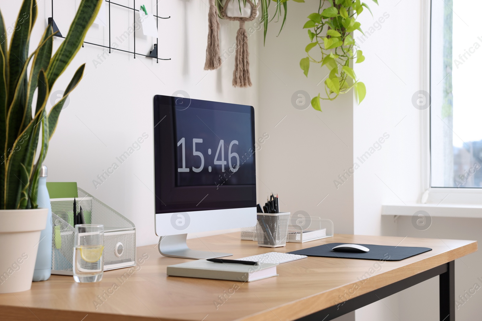 Photo of Cozy workplace with computer, modern furniture and houseplants at home