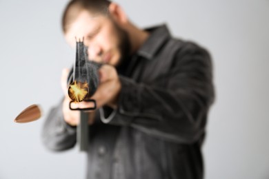 Image of Man shooting from assault rifle on light background, focus on weapon