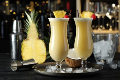 Photo of Tasty Pina Colada cocktails and ingredients on black wooden bar countertop