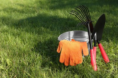 Photo of Metal bucket, gloves and gardening tools on grass outdoors, space for text