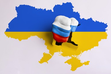 Russian aggression against Ukraine. Man breaking through map of Ukraine with fist painted in colors of Russian flag