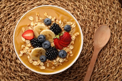 Photo of Delicious smoothie bowl with fresh berries, banana and oatmeal on woven mat, flat lay
