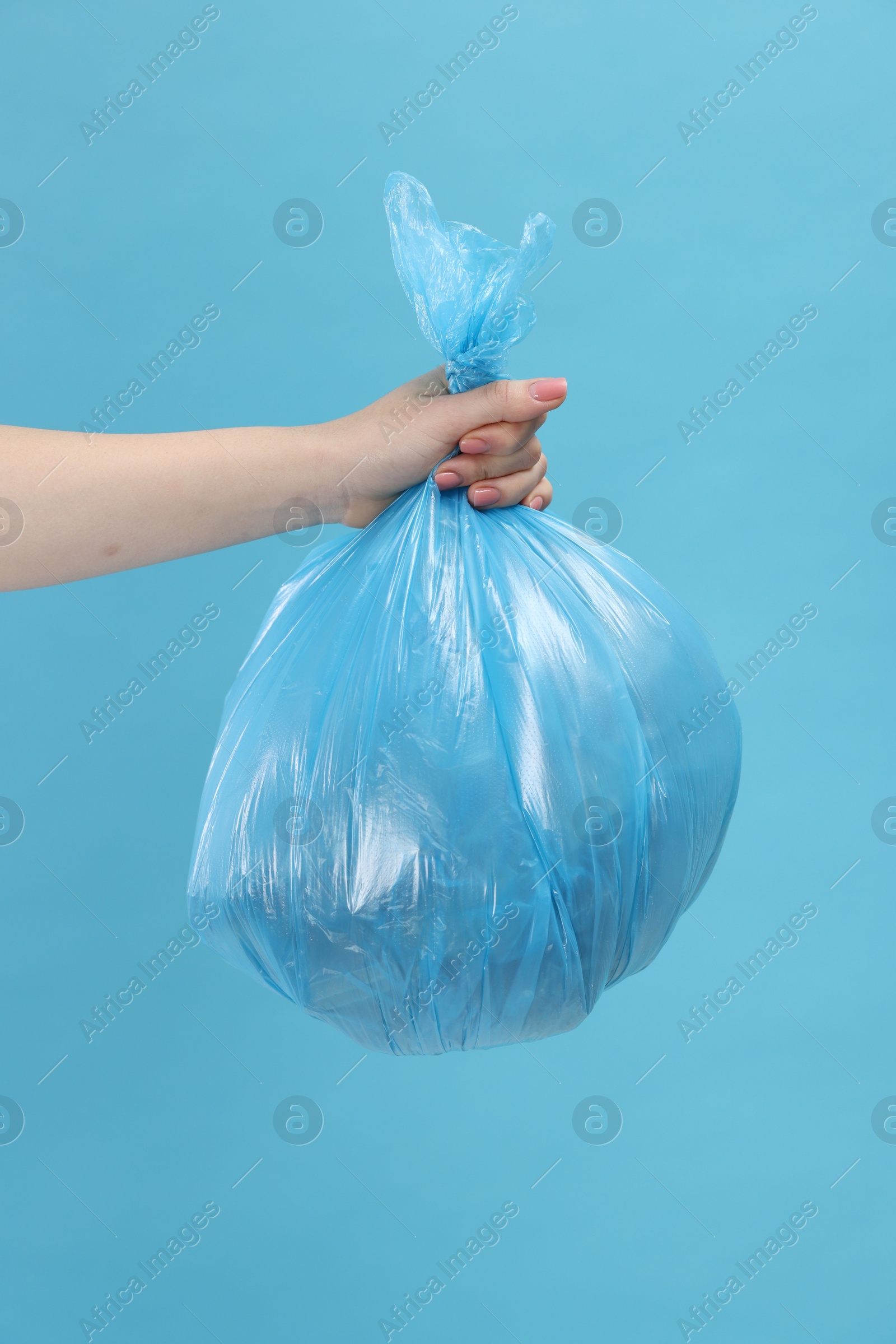 Photo of Woman holding plastic bag full of garbage on light blue background, closeup